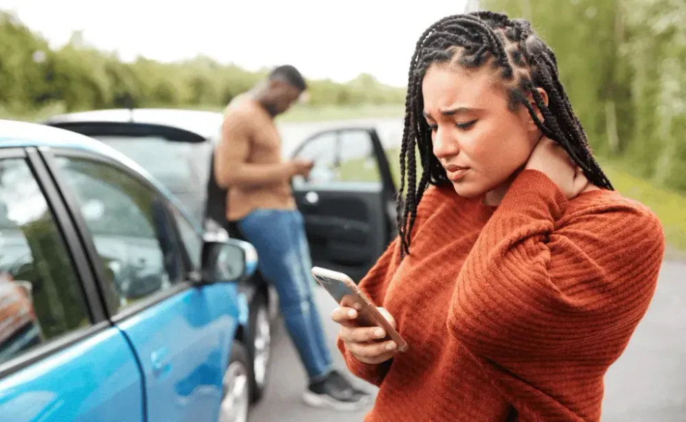 Woman Involved In Car Accident in Distress on Phone holding neck with crash in background